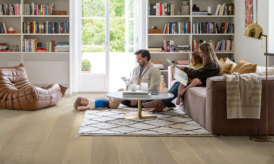 sala de estar con suelo de madera marrón y una familia sentada en el sofá leyendo